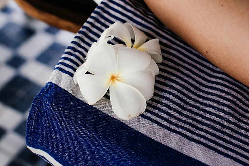 Deux fleurs blanches posées sur un tissu rayé bleu et blanc, avec une partie de la peau d'une personne visible en haut à droite.
