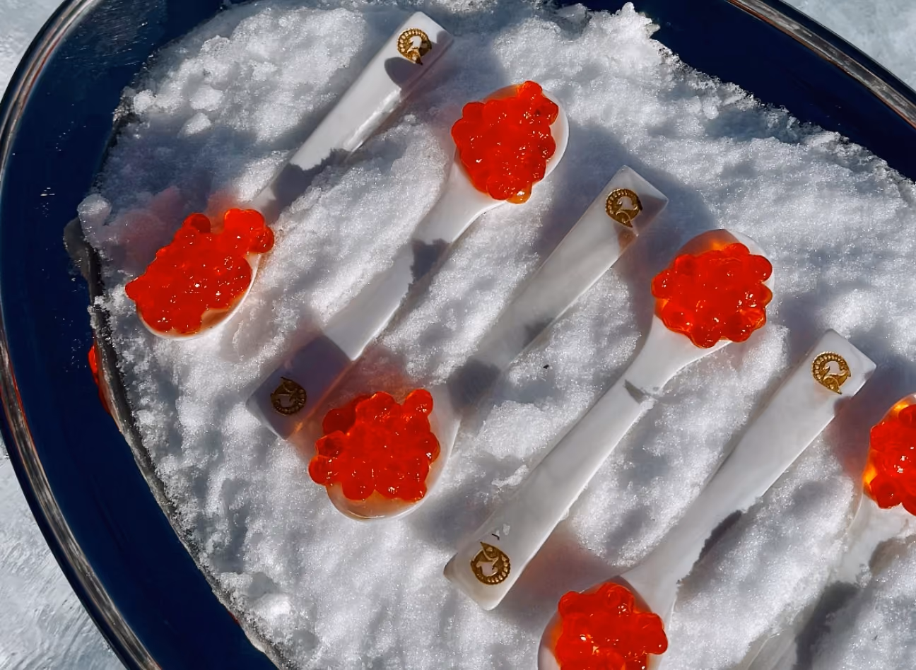 Gros plan sur un plateau en argenterie recouvert de neige, avec cuillères en nacre garnies d’œufs de saumon