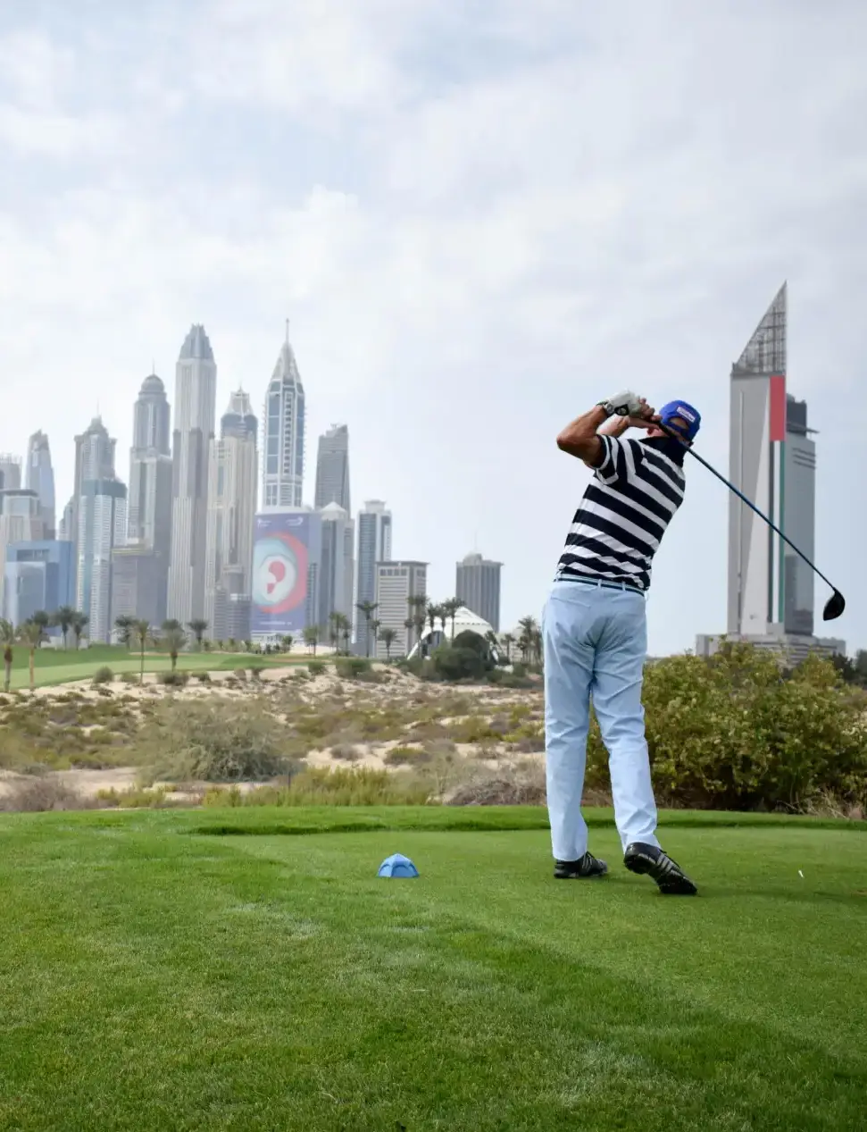 Young man wearing glasses and a black racing jacket sitting on the hood of a white and red Howdens sponsored race car outside a Howdens store.