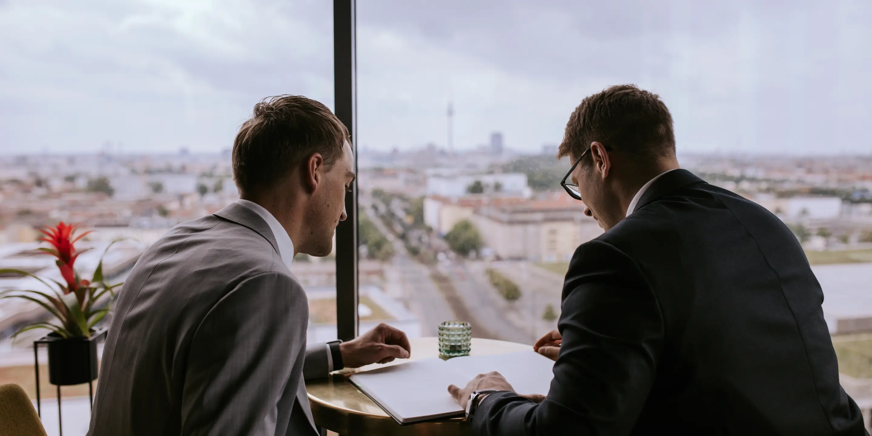 Five GRANIT business professionals in suits standing together in an office with large windows and city view.