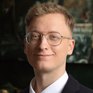Pierre Byhahn with glasses, light brown hair, and a slight smile wearing a dark blazer and white shirt.