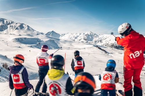 Groupe d'enfants en cours de ski avec un moniteur sur une montagne enneigée par une journée ensoleillée.