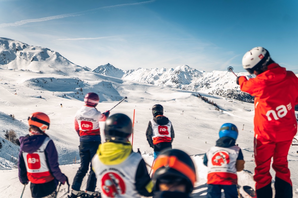 Groupe d'enfants en cours de ski avec un moniteur sur une montagne enneigée par une journée ensoleillée.
