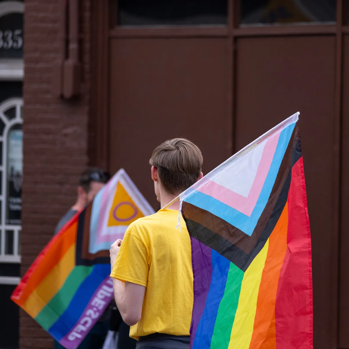 A person wearing a bright yellow shirt is facing away from the camera while holding a pride flag.