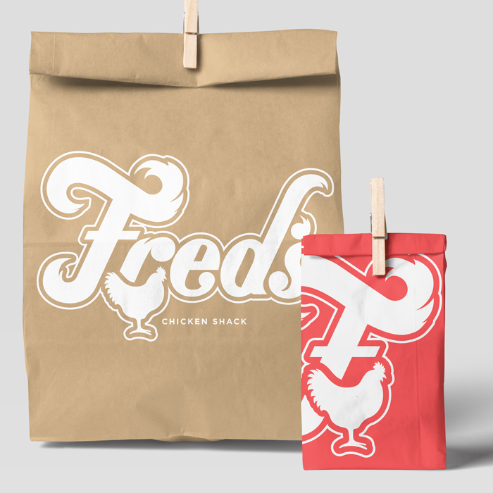 Two paper bags with clothespins, one large brown and one smaller red, featuring the word 'Fred's' with a chicken graphic and the text 'Chicken Shack'. Fred's logo.