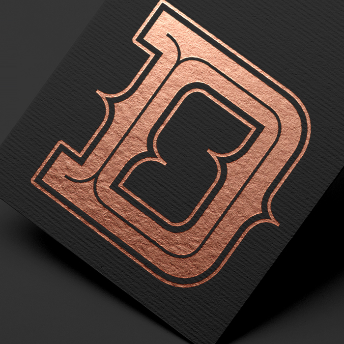 Copper-colored ornate letter D embossed on textured black paper. A simple logo with a D and and S.