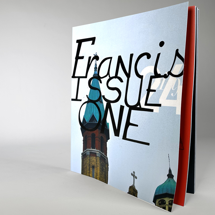 Francis Magazine Issue 1, standing upright with a cover showing a church steeple and the words 'Francis Issue One' overlaid in large black handwritten text.
