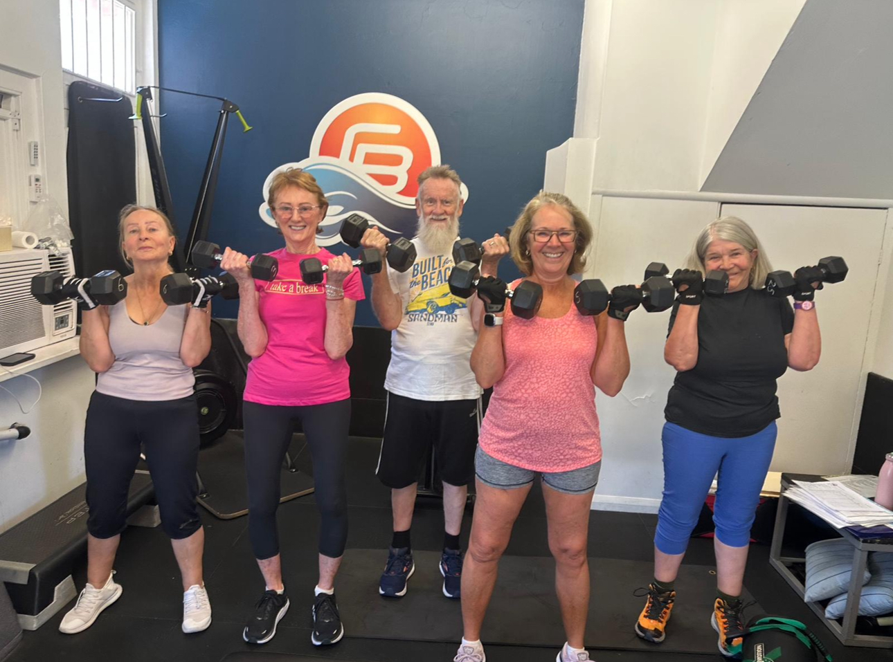 Group of older adults lifting dumbbells and smiling during a strength training session at Coastal Bodies gym in South Coogee