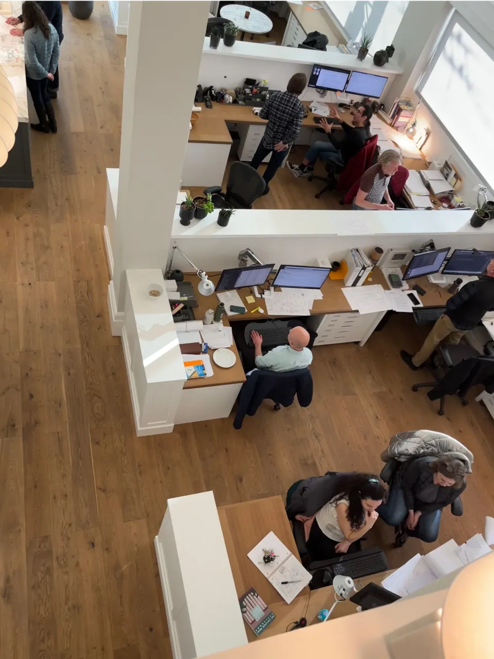 Overhead view of several people working and collaborating at desks in a modern office space.