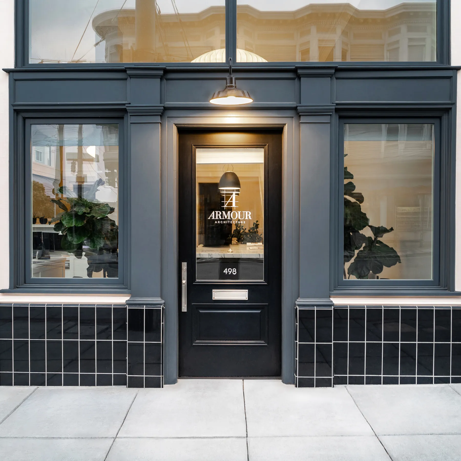 Black door entrance with Armour Architecture logo and number 498, flanked by two windows and plants inside.