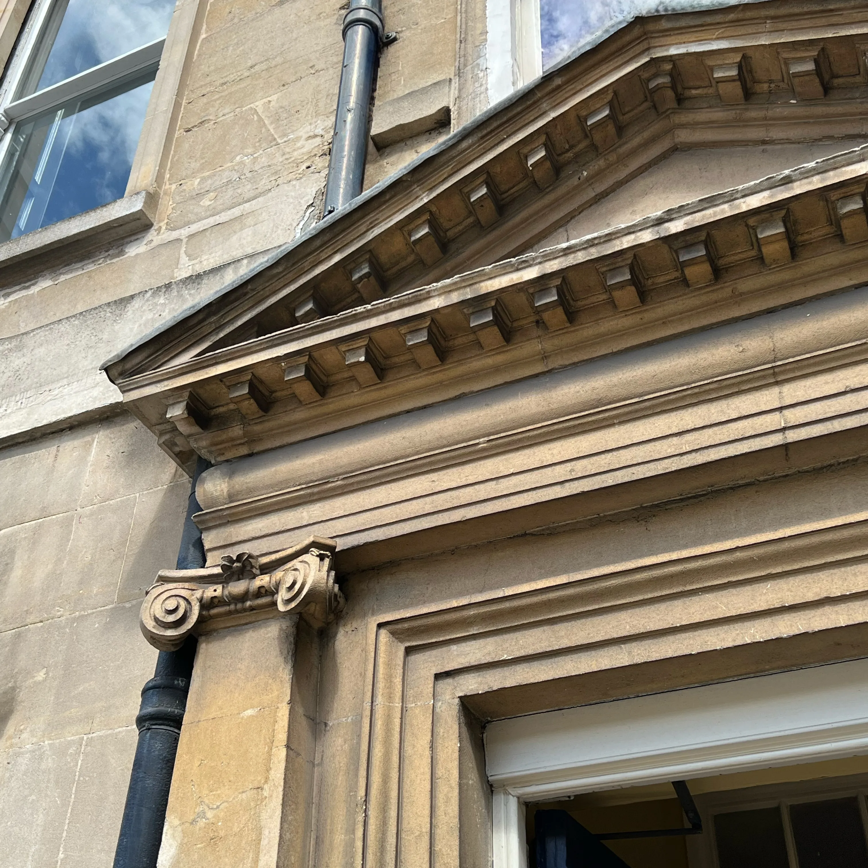 Close-up of a stone lintel with ornate carvings and dentil molding on an old building facade.