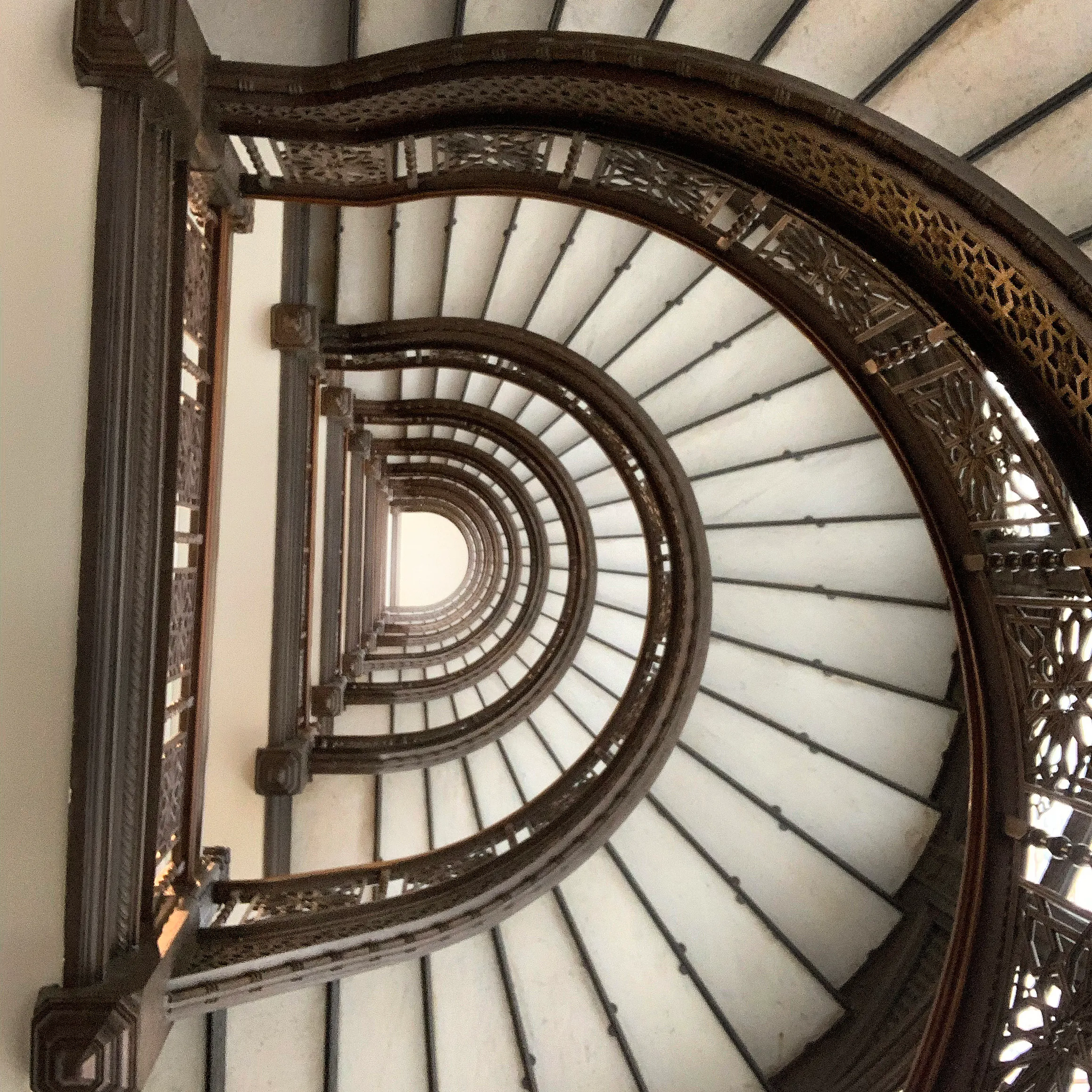 View looking up through a spiral staircase with ornate brown railings and white steps.