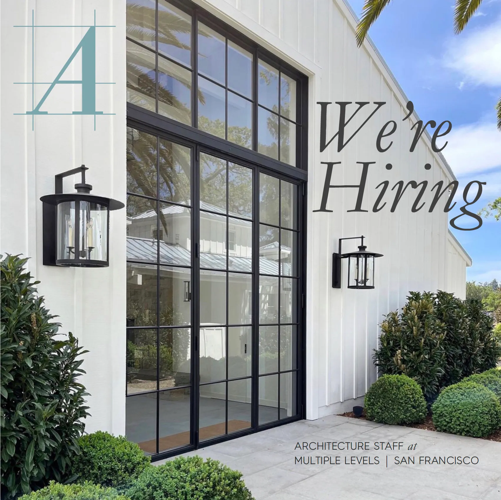 White building exterior with large black framed glass doors and greenery, text says 'We're Hiring.'