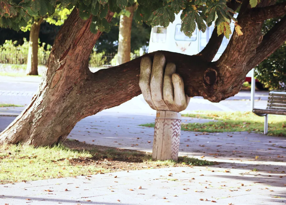 A big wooden hand holding up a tree branch.