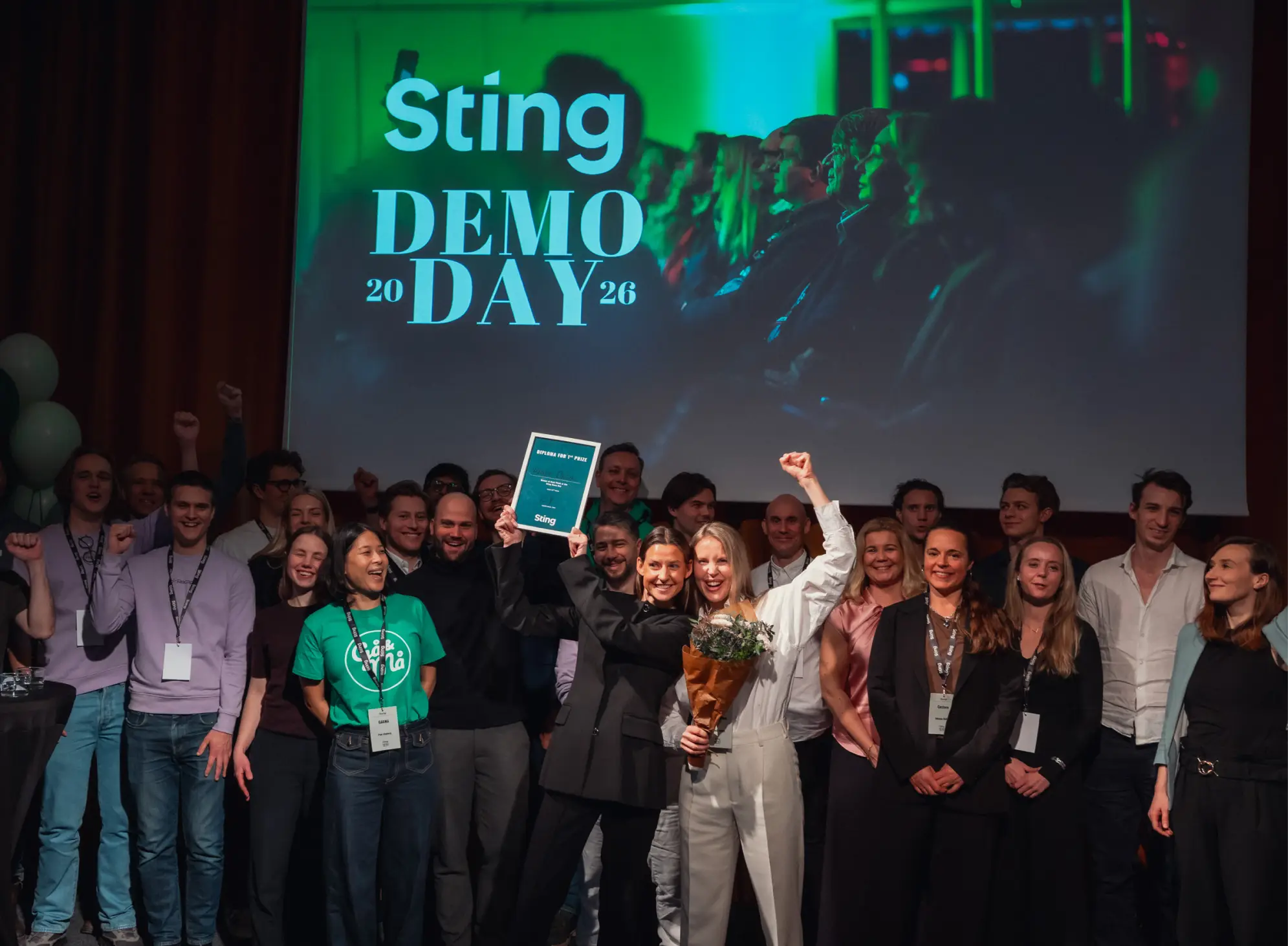 Two women from the Sting cohort 2025 celebrate on stage at Sting Demo Day 2026.