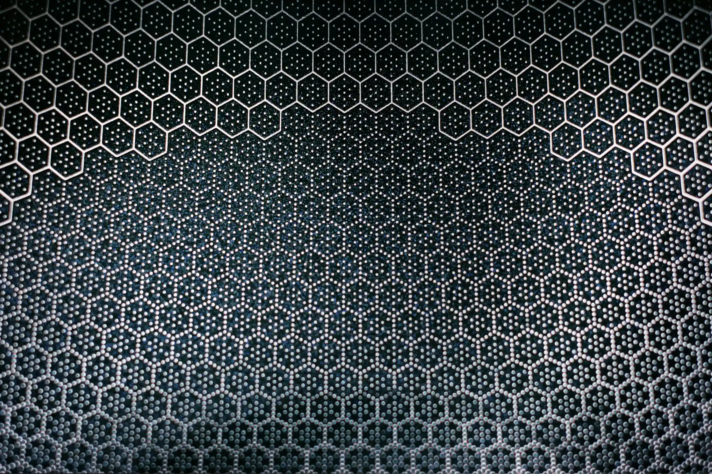 Close-up of a honeycomb pattern with hexagonal cells filled with small spheres on a dark surface.