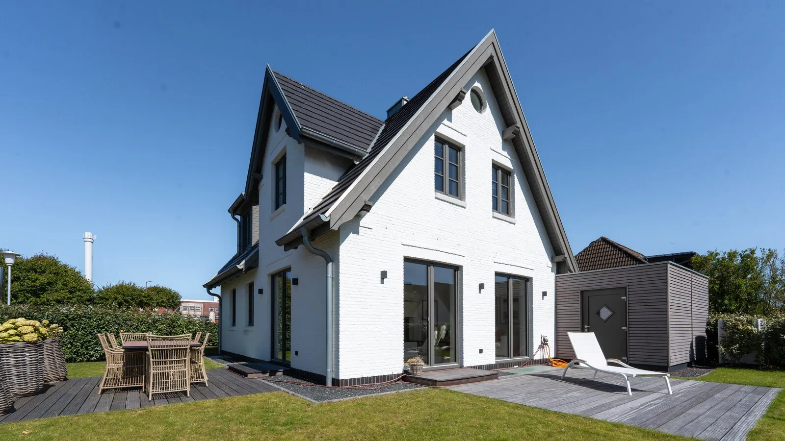 Weißes Friesenhaus mit Terrasse und Garten im Sonnenlicht