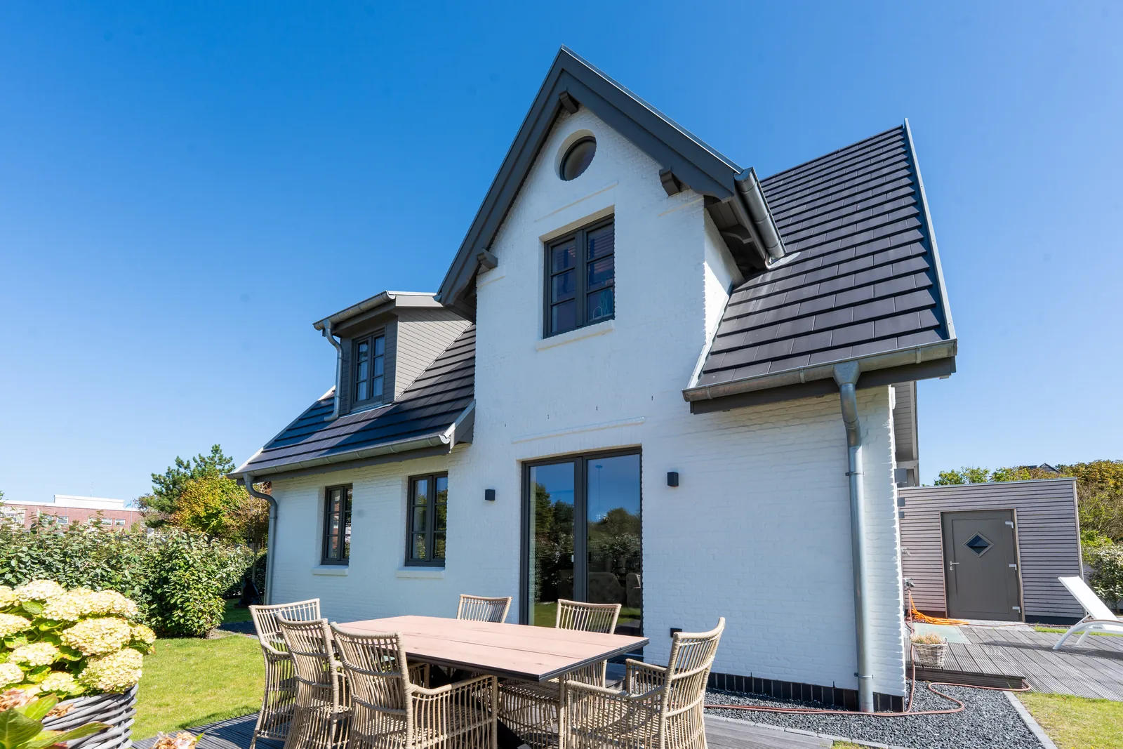 Weißes Friesenhaus mit Terrasse, Esstisch und Hortensien im Garten