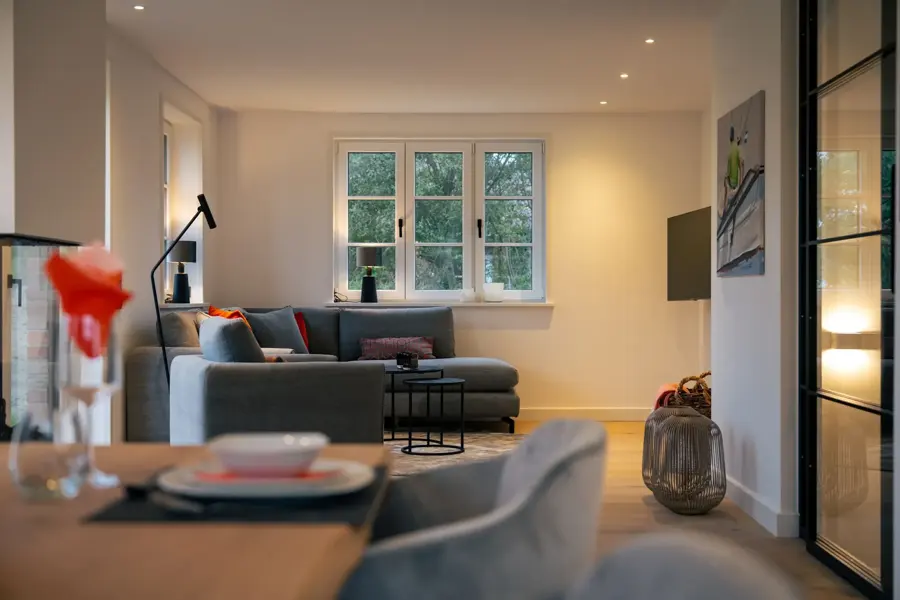 Wohnbereich mit grauem Sofa und gedecktem Tisch am Sprossenfenster