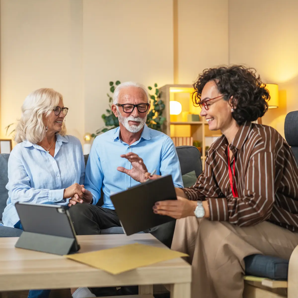 Une ergothérapeute de chez Aid'habitat montre un rapport  d'autonomie à un couple de personnes âgées assis sur un canapé dans un bureau lumineux.