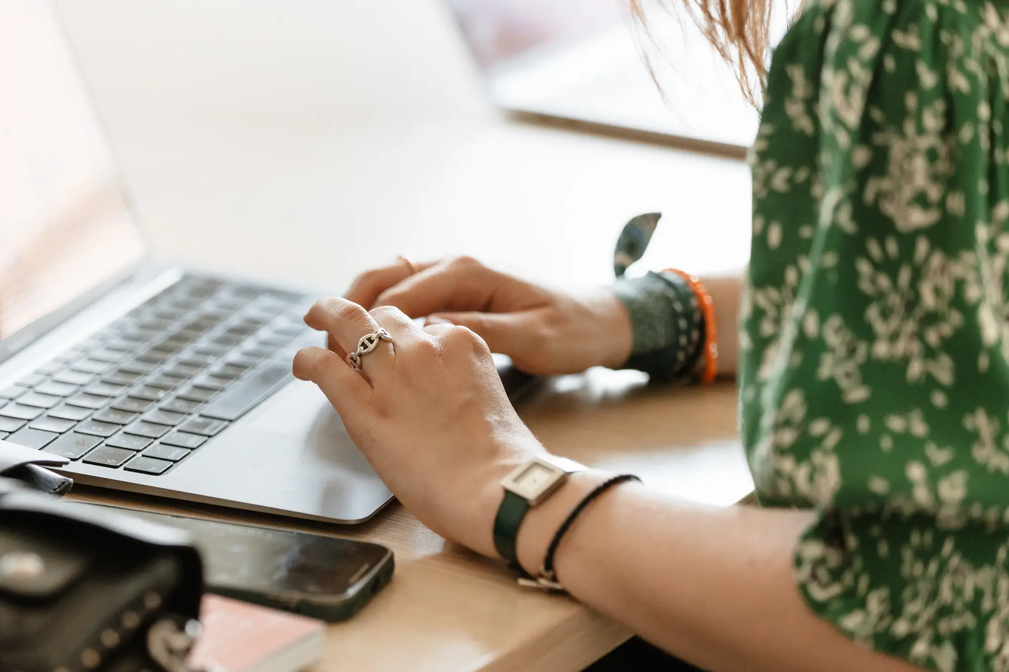 Mains d'une personne tapant sur un ordinateur portable posé sur un bureau afin d'obtenir des informations sur la rénovation énergétique avec un téléphone portable et un sac à proximité.
