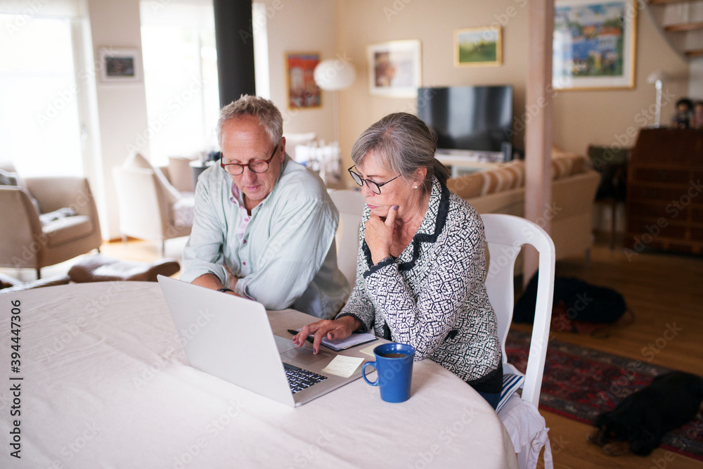 Un couple de personnes âgées assis à une table ronde se renseignant sur les aides possilbe pour l'adaptation de leur logement dans un salon lumineux.