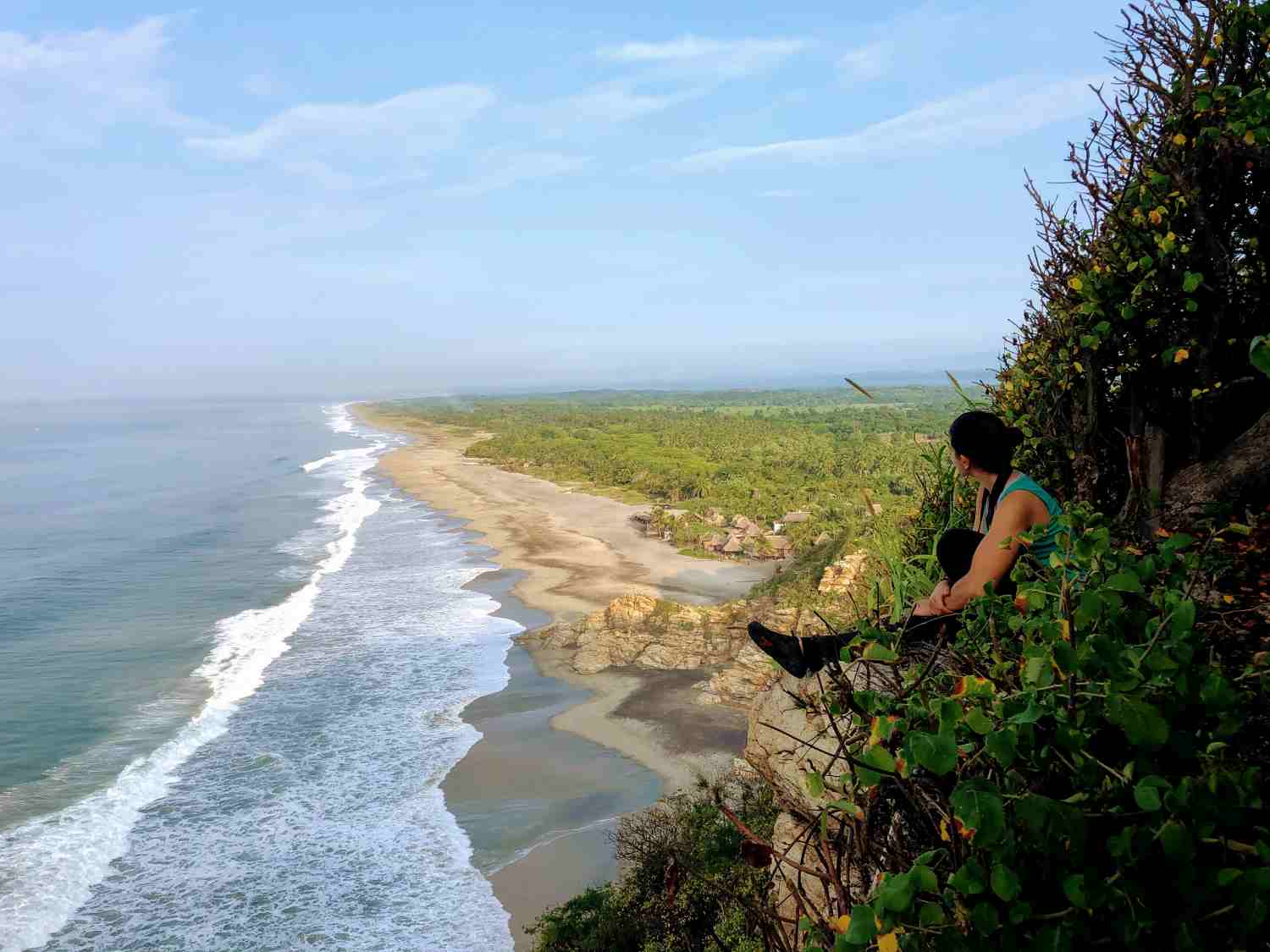 Voyageur assis sur une falaise avec plage et végétation à Playa la Ventanilla, Oaxaca