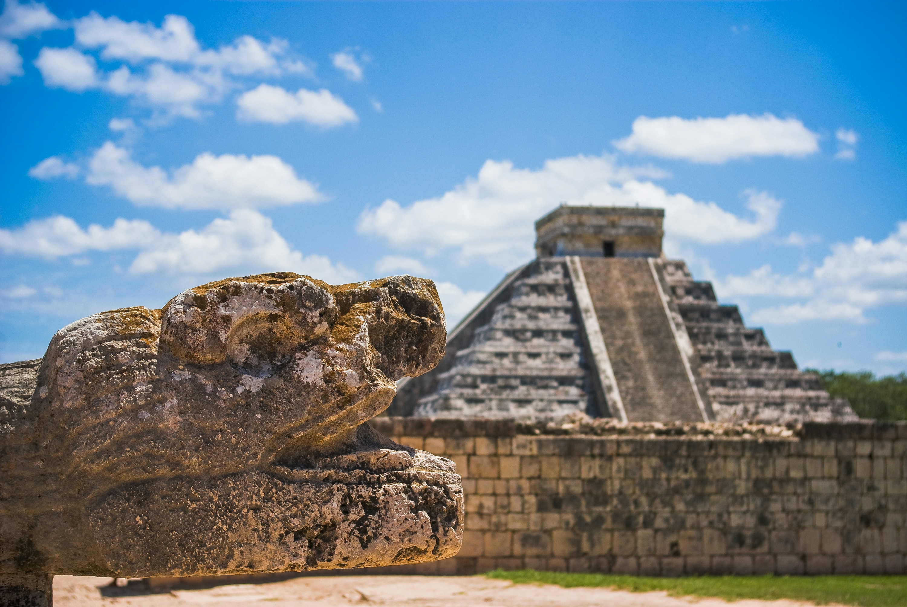 A Chichén Itzá Tour Guide from Cancún, Tulum, and Playa – Serpent head sculpture with El Castillo in the background.
