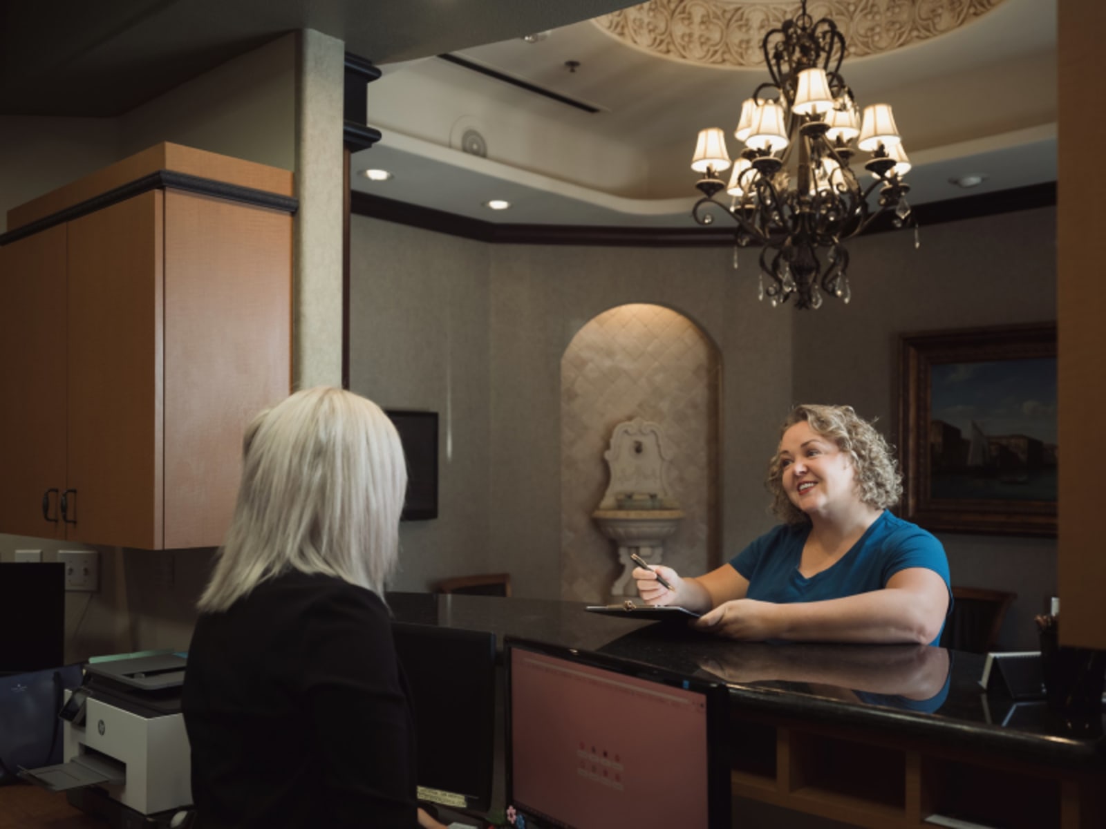 Female dental professional at reception desk with warm, professional demeanor