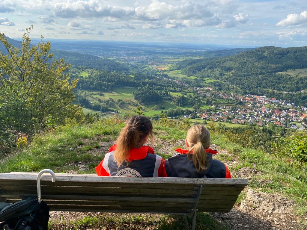 Two woman sitting on a bench looking on a valley