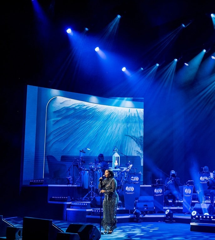 a woman singing on a stage with a band on it