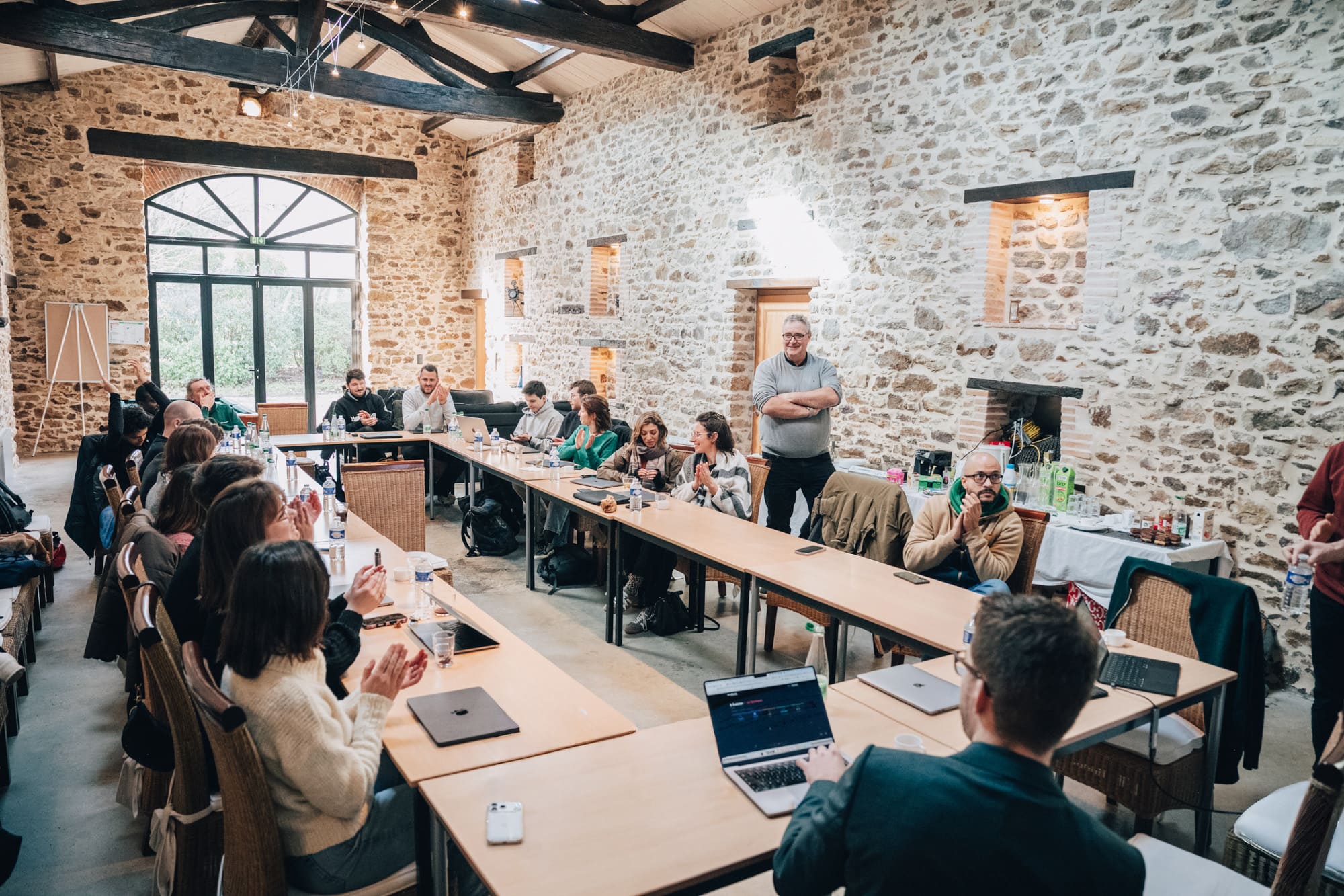 Un groupe de personnes assises dans une salle avec des murs en pierre, discutant autour de tables en U.