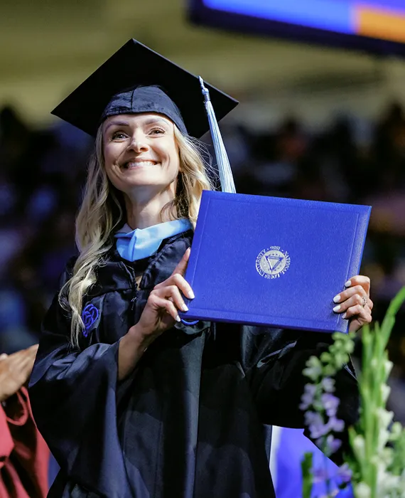 A woman in a cap and gown holding a blue diploma.