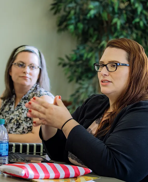 Two women sitting at a table with a laptop.