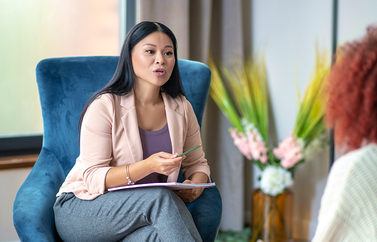 A woman sitting in a blue chair talking to another woman.