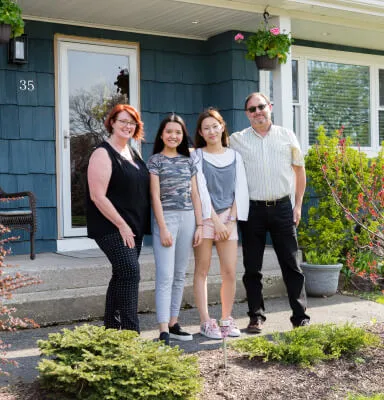 A diverse family of four standing outside a blue house with the number 35 beside the door.
