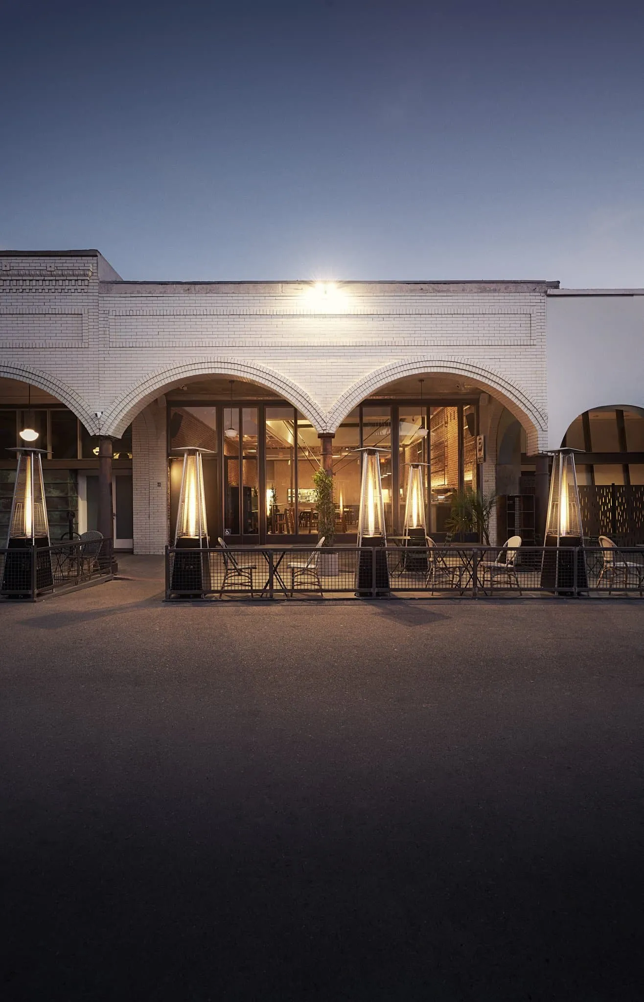 Market restaurant exterior at twilight with arched windows and glowing patio heaters