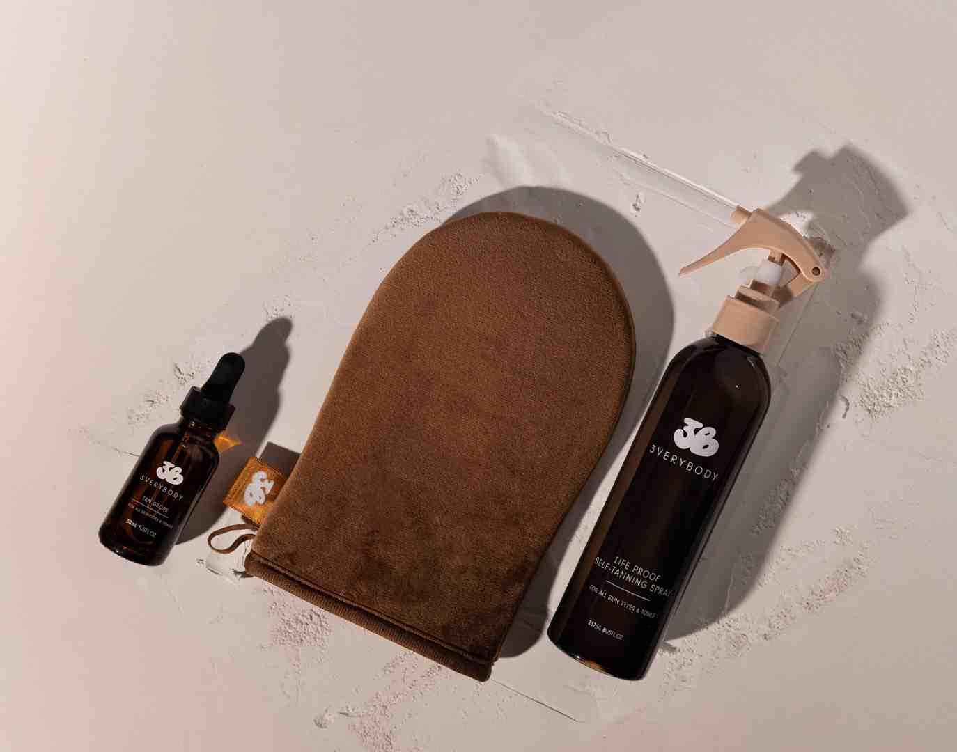 clear Tinted Tanning Water being spritzed onto the 3VERYBODY Tanning Mitt. - self tanner no transfer