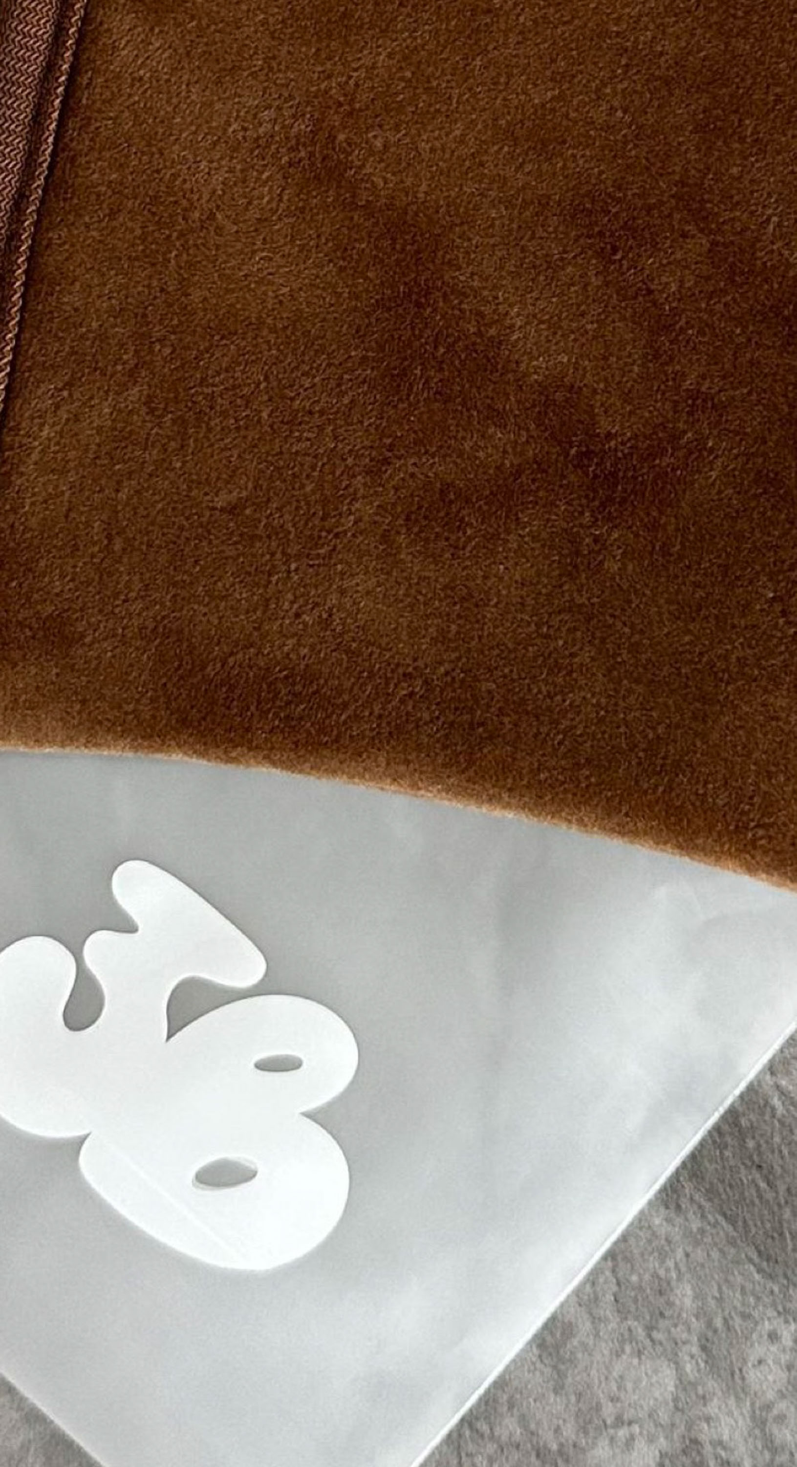 Close-up of the plush brown 3VERYBODY tanning mitt and its logo