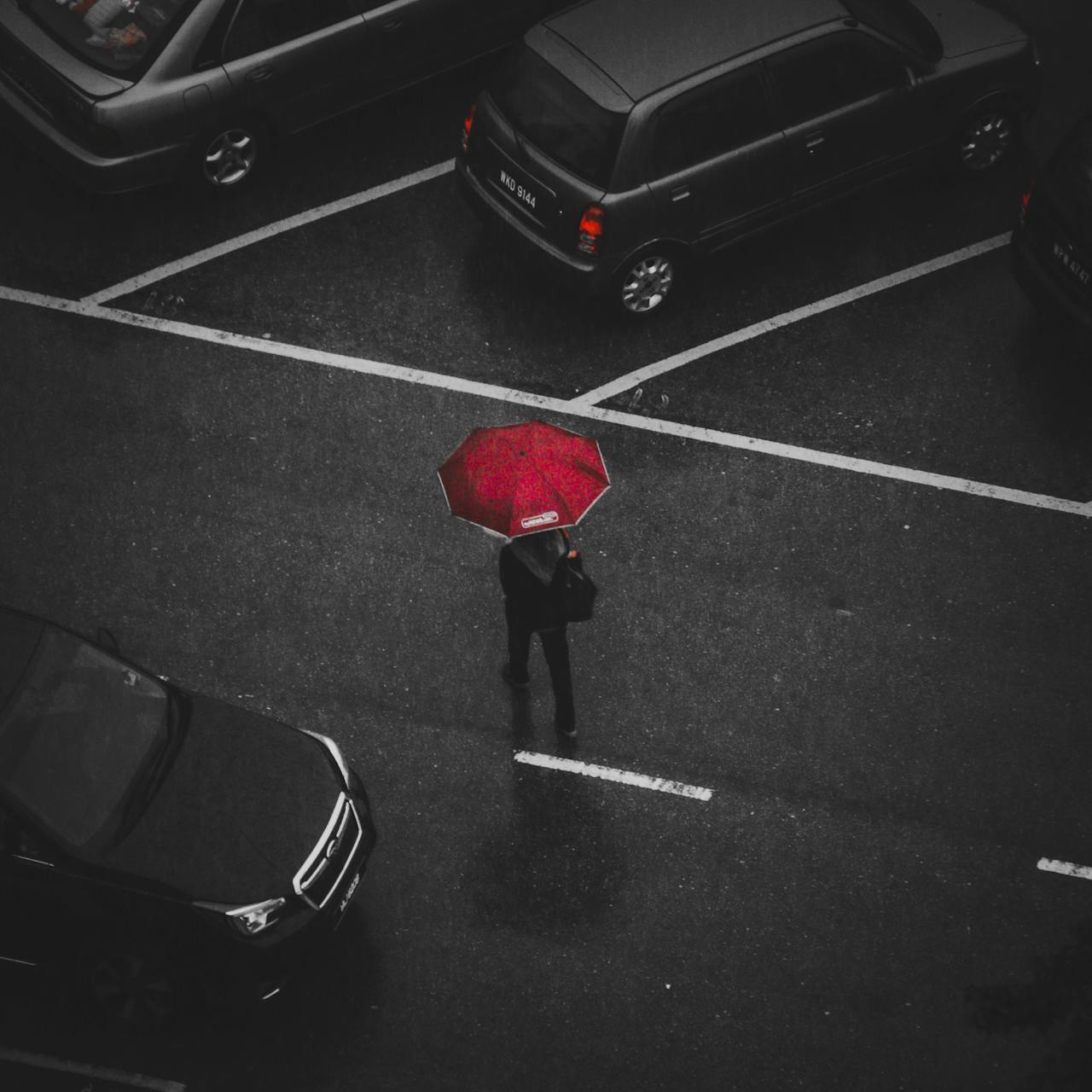 A person in a parking lot under a red umbrella 