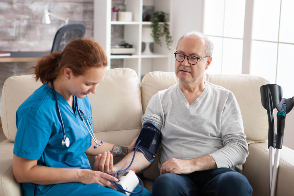 lady in blue scrubs performing a blood pressure check on a man wearing glasses