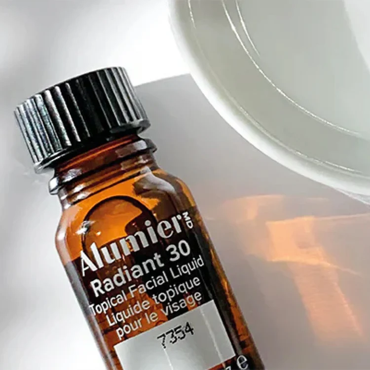 Amber glass bottle of Alunier MD Radiant 30 topical facial liquid with black cap next to a white ceramic plate.