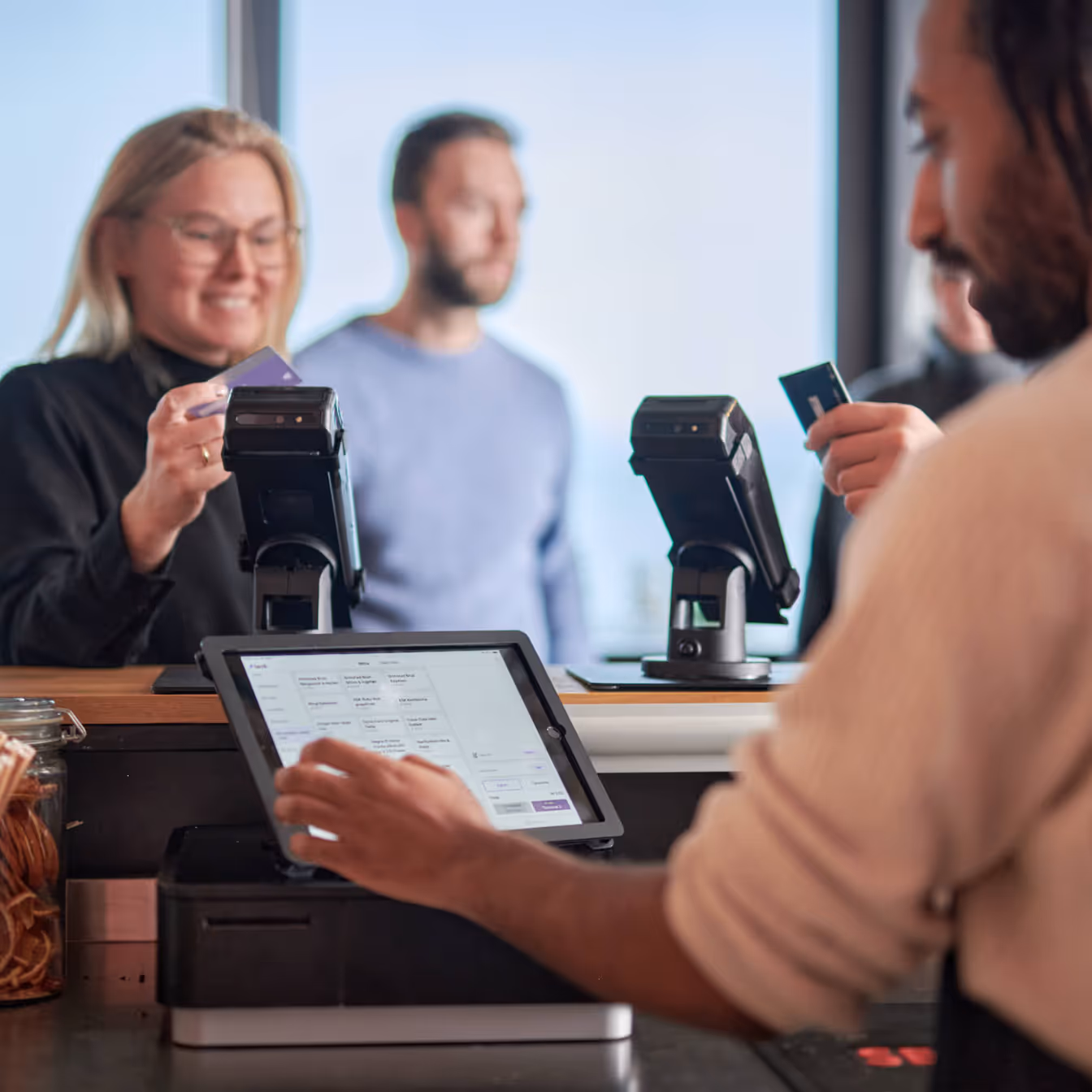 Smilende jente i 30 årene betaler med kort i baren hvor en smilende bartender taster inn ordre på Favrit kassesystem