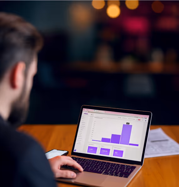 Mann som ser på en bærbar datamaskin med et økonomisk søylediagram på skjermen i et dempet, innendørs miljø.