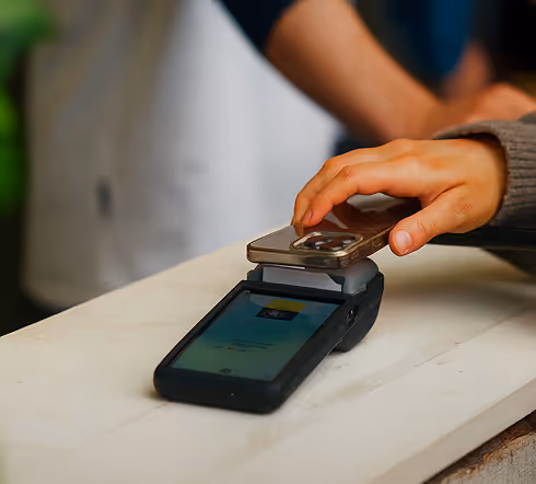 Person bruker mobiltelefon til kontaktløs betaling på en betalingsenhet over disken.