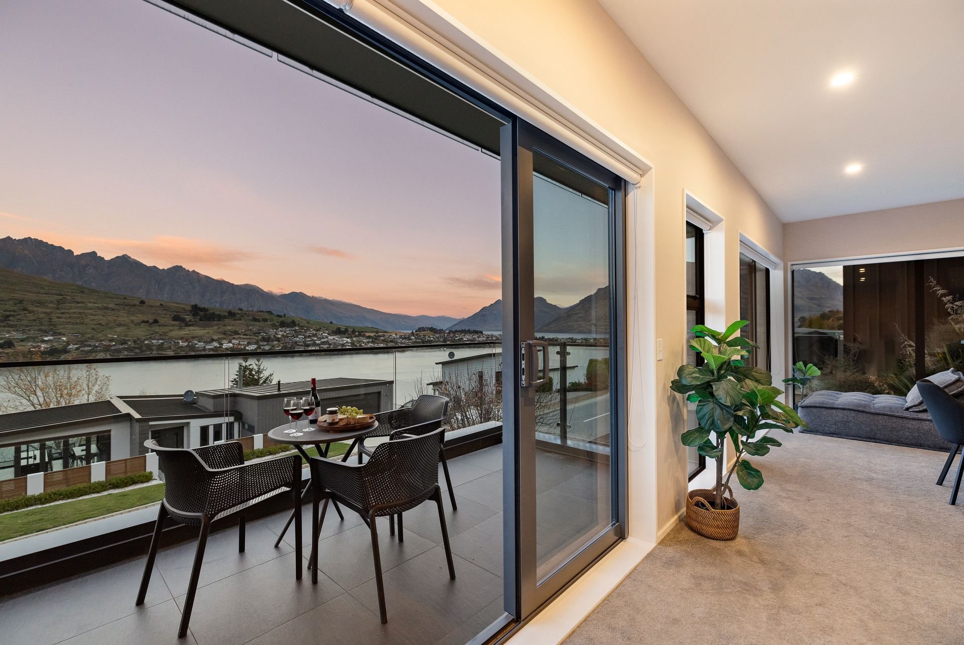 Balcony dining table at sunset seen through the sliding doors at Cecil Peak House, Queenstown