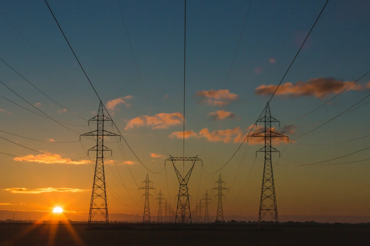 High-voltage transmission towers and power lines crossing open land at sunset