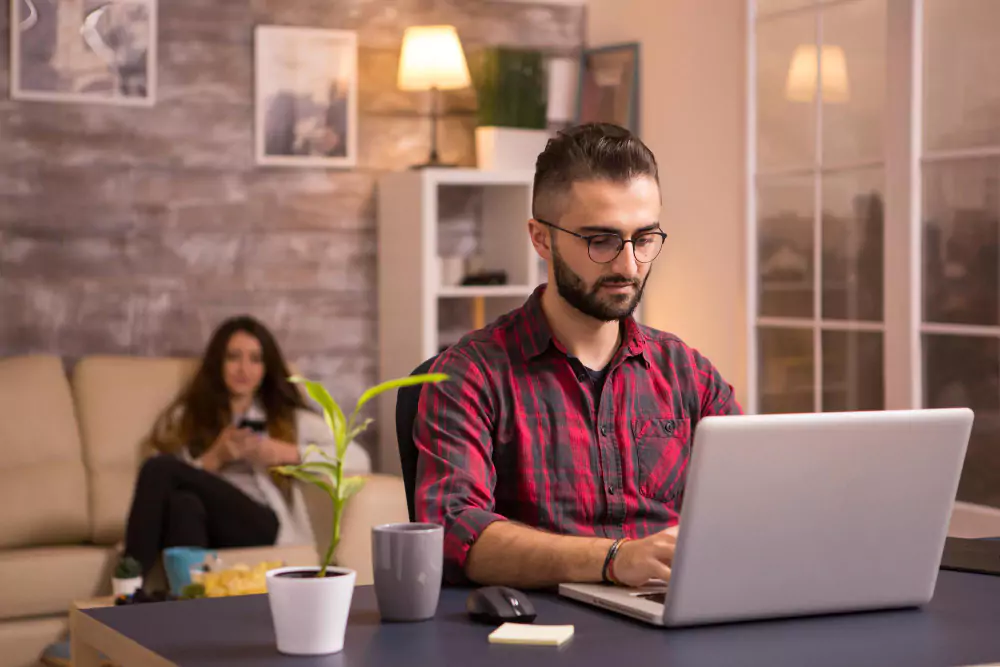 Trabajador independiente con barba trabajando con una computadora portátil en la sala de estar