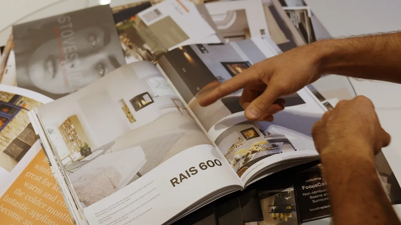 Person pointing at an open catalog showing images and details of the RAIS 600 fireplace.