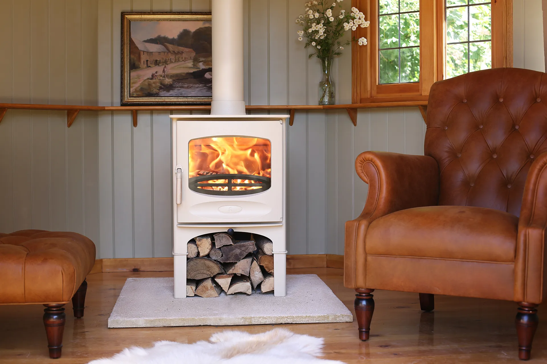 Cozy living room with a white wood stove burning firewood between two brown leather chairs.